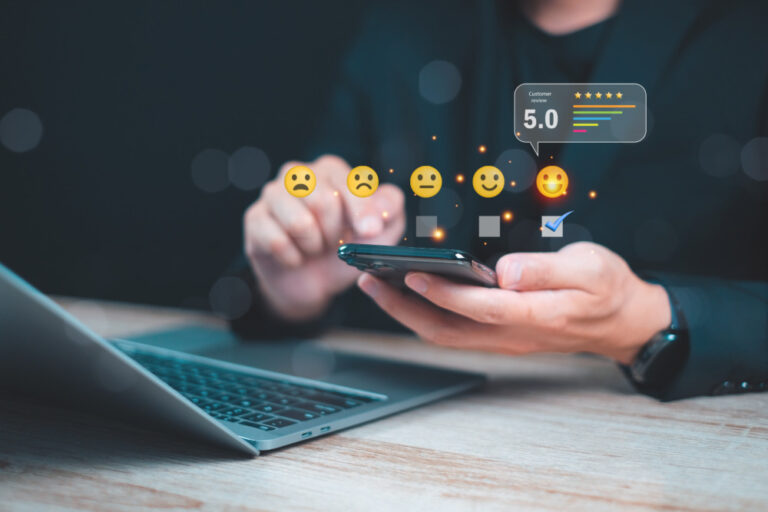 competitor analysis mobile shown by person using a smartphone to provide feedback and ratings with emoji icons while working on a laptop, concept of online review and customer feedback.