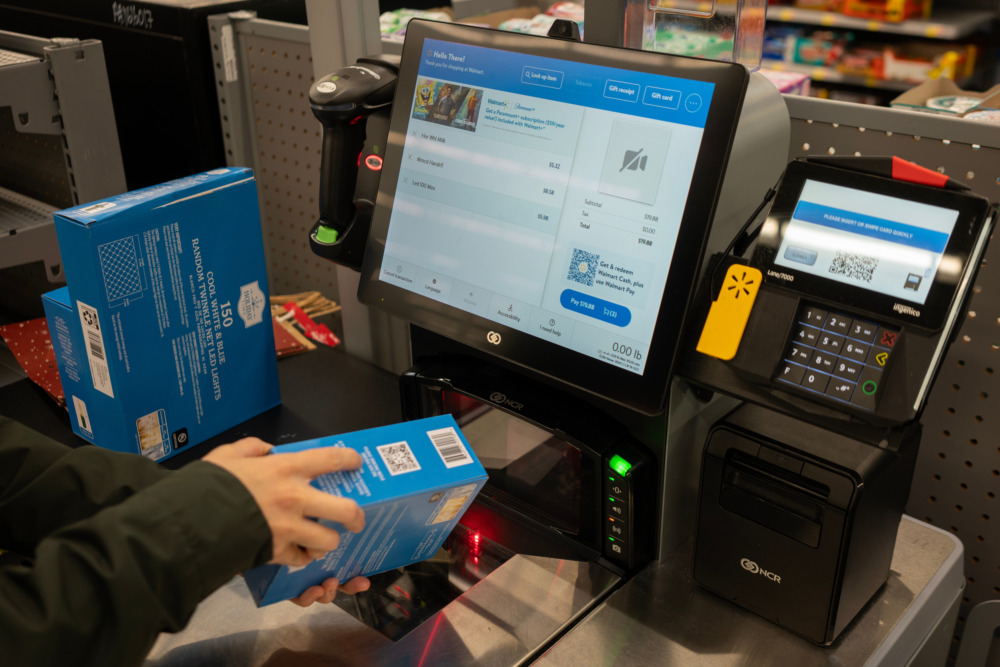 A shopper scans a product barcode on packaging at the self-checkout lane in a Walmart