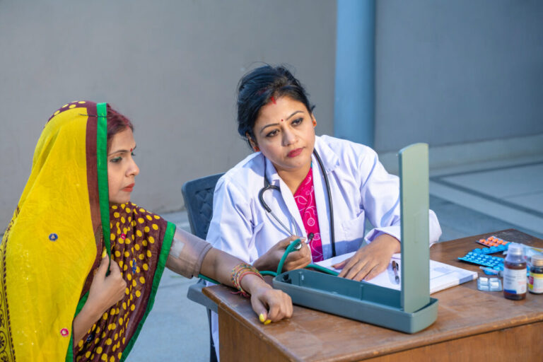 Oracle Health Community Care shown by Indian female doctor checking blood pressure of rural woman at clinic