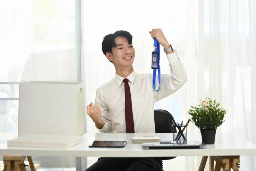 Excited male employee celebrating new job with ID badge in hand