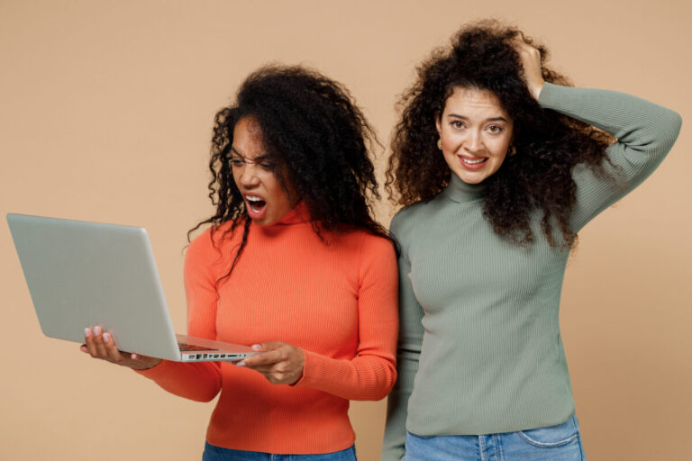 VPN protecting your identity illustrated by two puzzled young curly black women friends 20s holding a laptop pc while one looks shocked and the other bemused