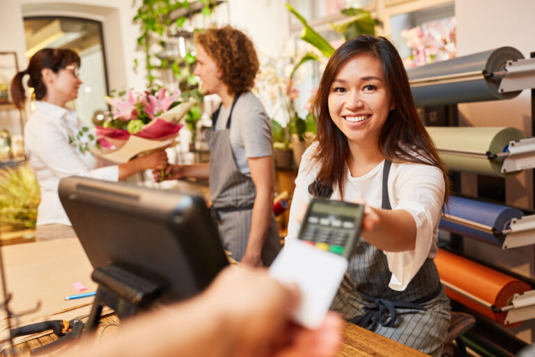 HPE Retail solutions shown by smiling young cashier holding out card machine to customer