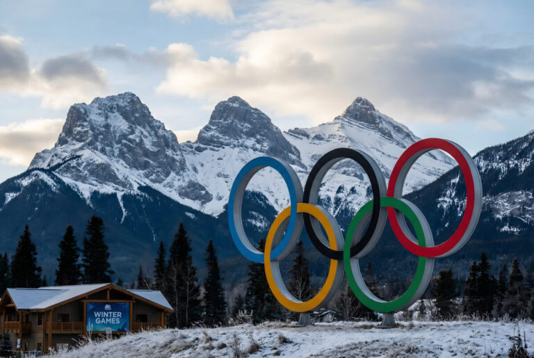 Olympic Rings Monument Against Snowy Mountains and Winter Games Building