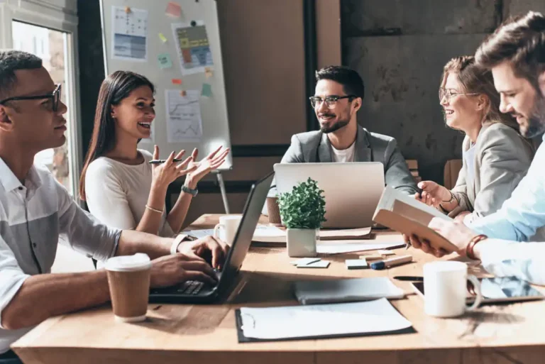 business notebook mistakes shown by people working together. Group of young modern people in smart casual wear discussing business and smiling while sitting in the creative office
