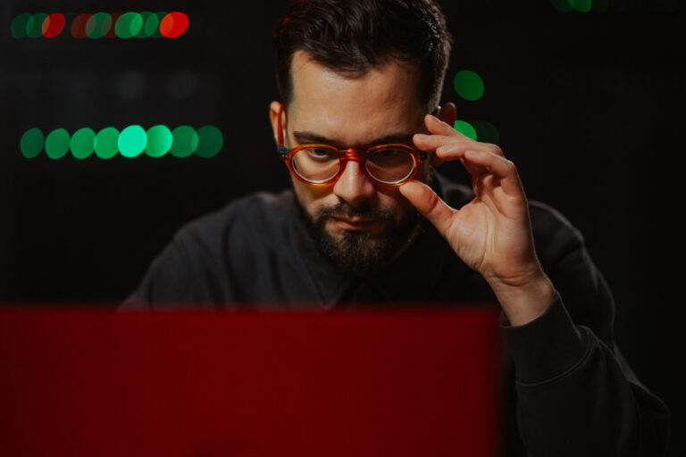 trust security vendor - difficulty shown by male it specialist wearing glasses, concentrating while working on a laptop in a data center, surrounded by server lights