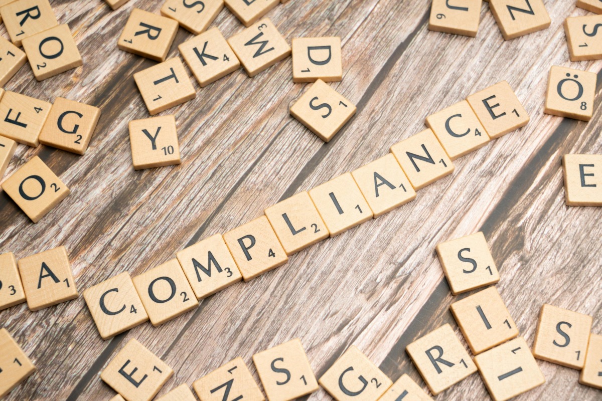 CISO compliance strategy - Wooden letter tiles forming the word 'COMPLIANCE' on a rustic wooden background.