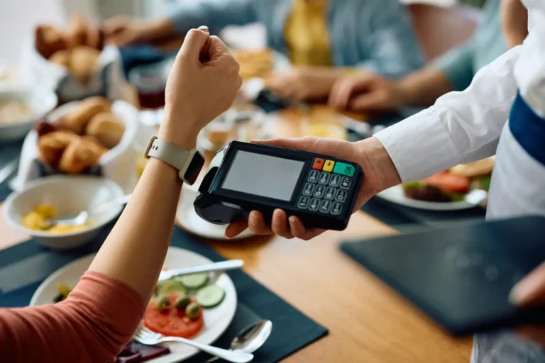 paying bills abroad shown by woman using contactless watch to pay for a bill