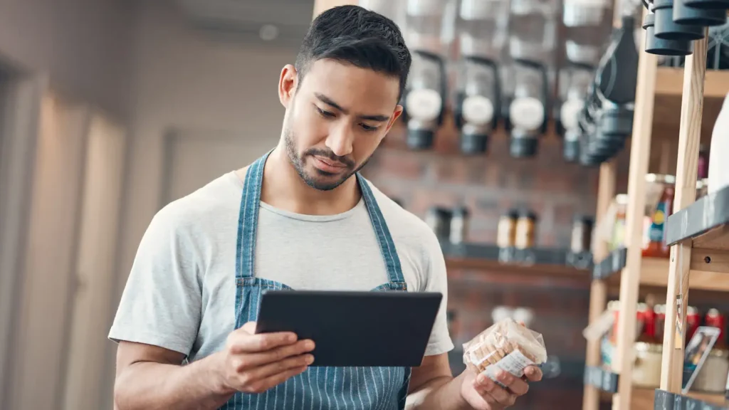 male worker undertaking stock management in shop - looking at tablet whilst holding jar